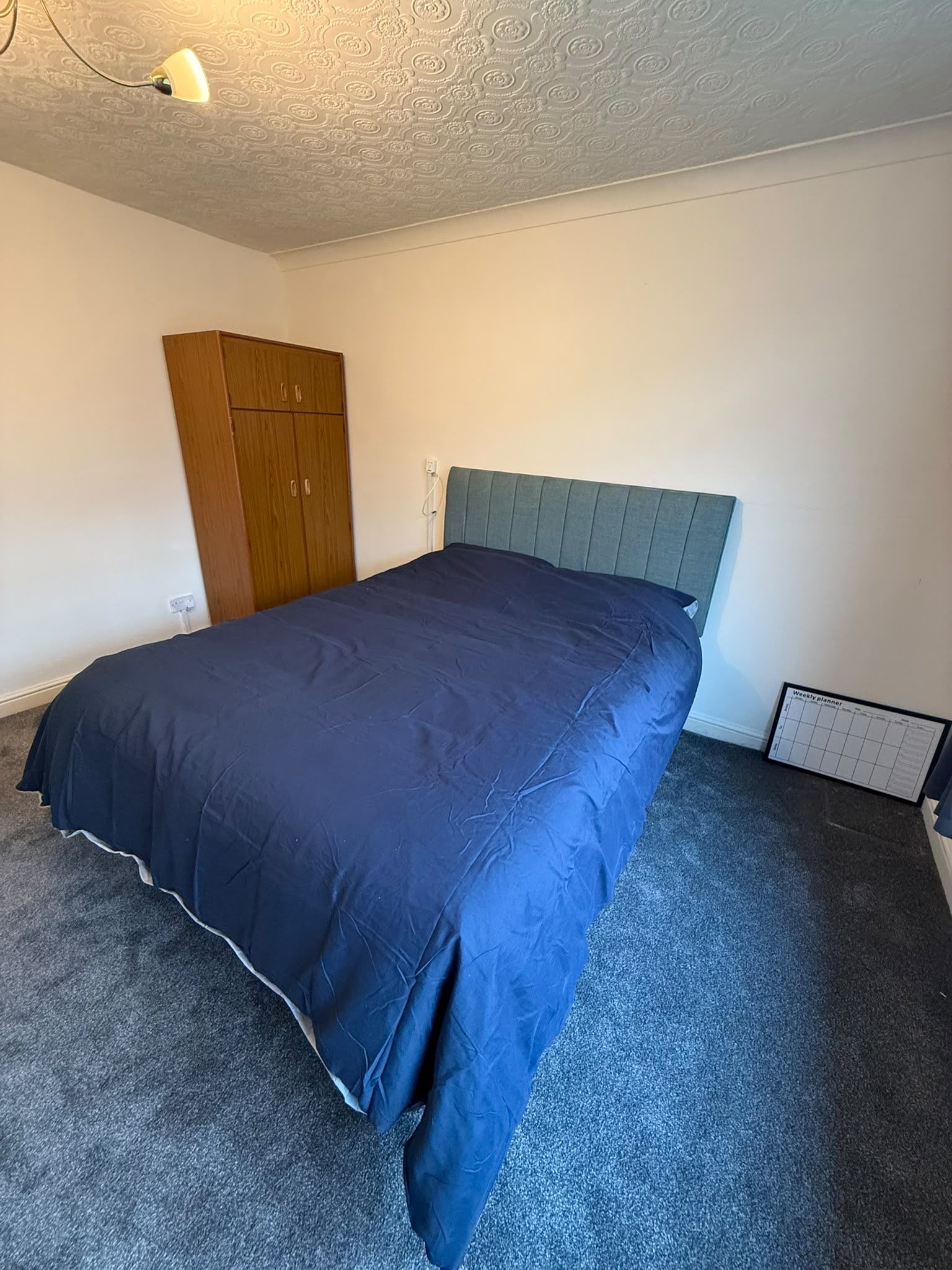 Quarto com cama, guarda-roupa e luminária na parede.