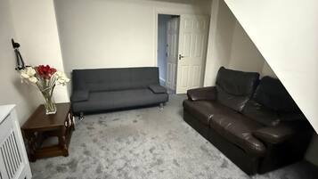 A living room with a grey carpet, two sofas, a small wooden table with a vase, and a white door.