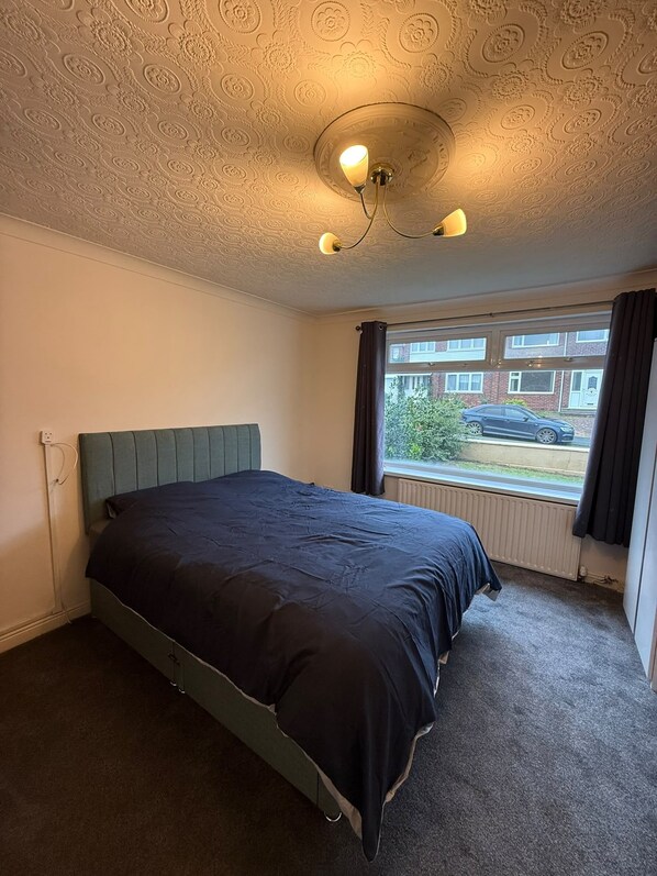 A bedroom with a single bed, a window with curtains, and a patterned ceiling.