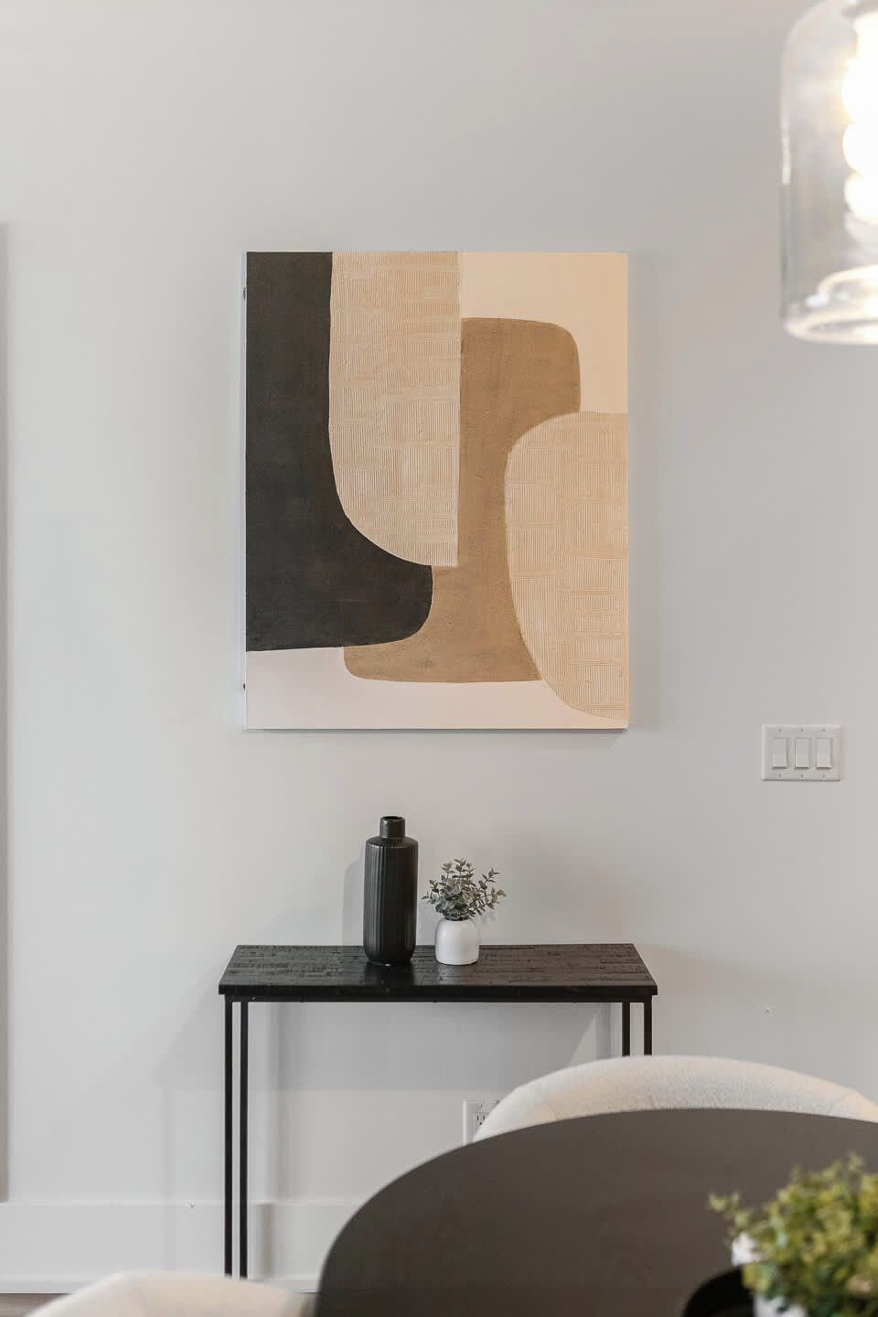 A modern interior with a minimalist wall art piece, a small table with a vase, and a dark-colored sofa.