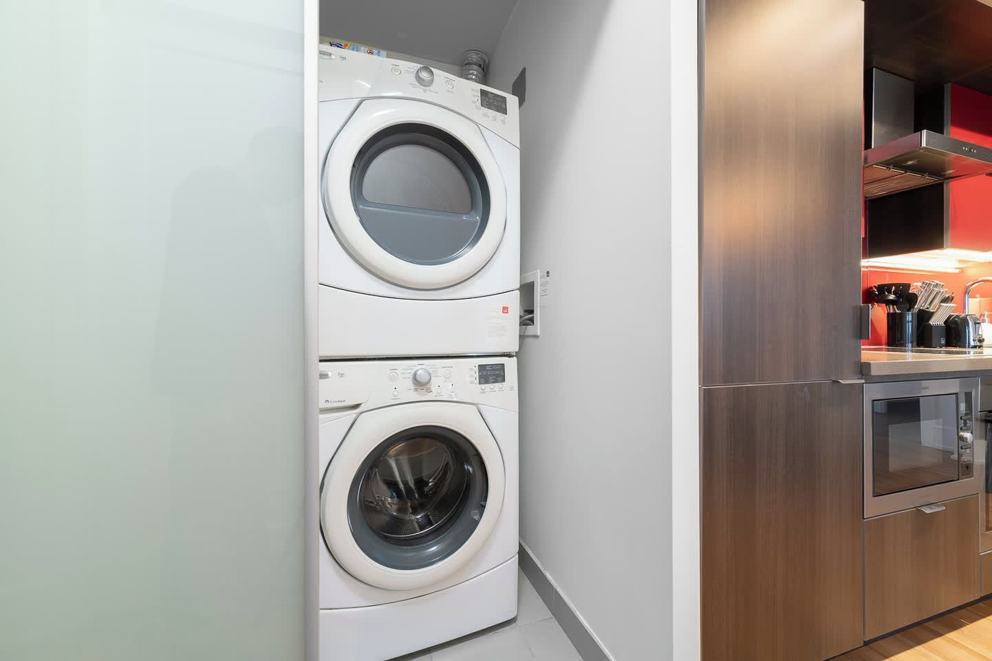A compact laundry room with two stacked washing machines and a modern kitchen area with stainless steel appliances.