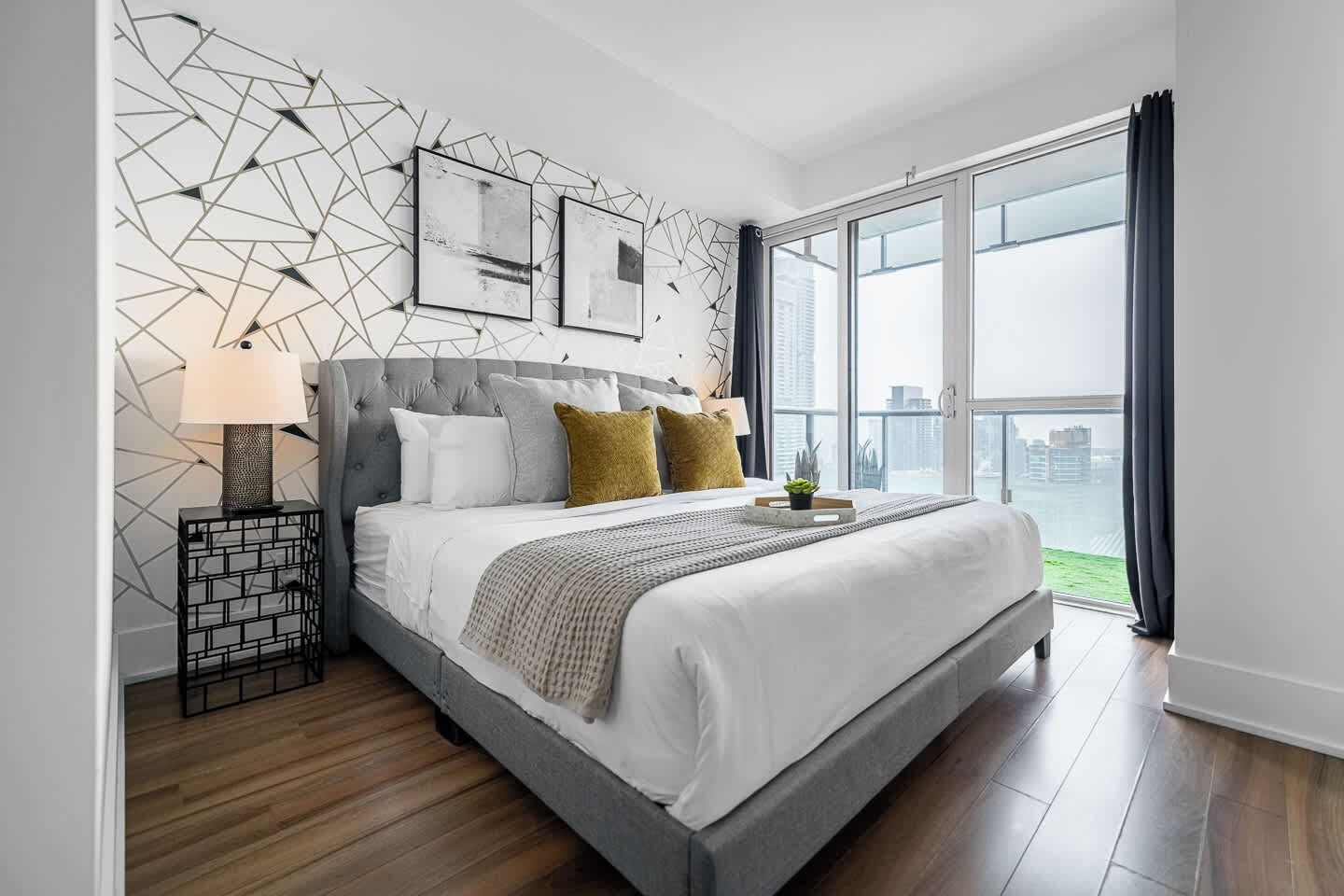 A modern bedroom with a large bed, a geometric wall design, and a city view.