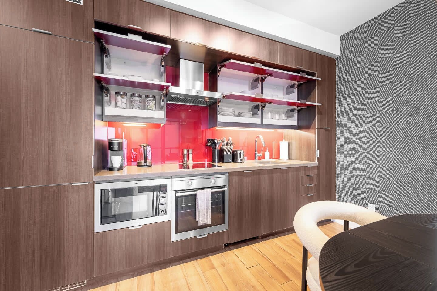 A modern kitchen with built-in appliances, a red backsplash, and a wooden floor.
