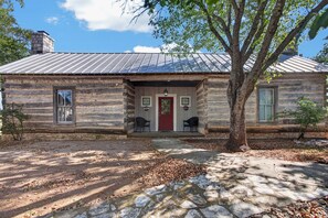A log cabin with a stone foundation, a metal roof, and a front porch with two chairs. - Cabin w/King bed on Wine Trail, Walk to Wineries! (Fredericksburg)
