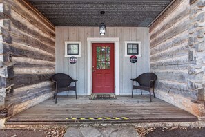 Eine Blockhütte mit roter Tür, zwei Korbstühlen und einer Veranda mit Fußmatte.