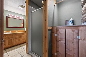 Ein Badezimmer mit Holzwaschtisch, einem beleuchteten Spiegel, einer Duschkabine und Fliesenboden.