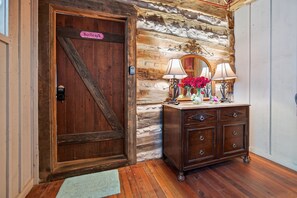 A wooden door with a sign, a stone wall, a wooden dresser with lamps, and a mirror. - Cabin w/King bed on Wine Trail, Walk to Wineries! (Fredericksburg)