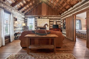 A rustic log cabin interior with a wooden table, leather sofa, and a horse sculpture. - Cabin w/King bed on Wine Trail, Walk to Wineries! (Fredericksburg)