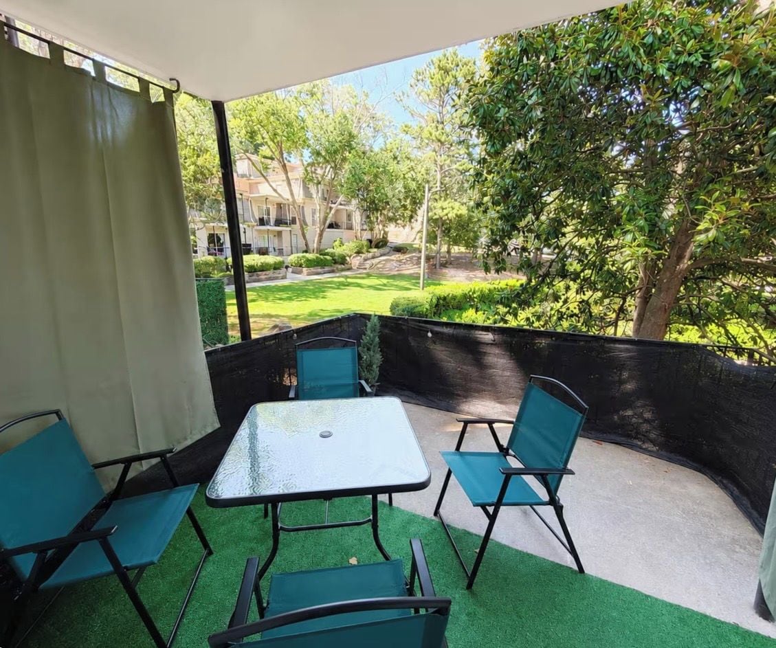 Un espacio de estar al aire libre cubierto con una mesa y sillas, rodeado de follaje y vistas de edificios.