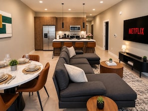 A modern living room with a sectional sofa, a dining area with a round table, and a kitchen in the background. - Skyline Nook | 2BR Downtown Stay (Birmingham)
