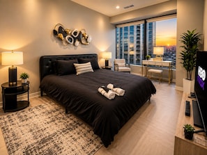 A modern hotel bedroom with a large bed, bedside tables, a desk with a chair, and a city view. - Skyline Nook | 2BR Downtown Stay (Birmingham)
