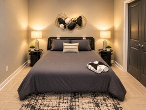 A bedroom with a large bed, two bedside tables with lamps, a wall-mounted decorative piece, and a door. - Skyline Nook | 2BR Downtown Stay (Birmingham)