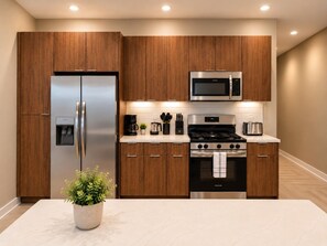 A modern kitchen with wooden cabinets, stainless steel appliances, and a marble countertop. - Skyline Nook | 2BR Downtown Stay (Birmingham)