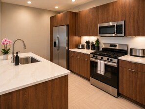 A modern kitchen with stainless steel appliances, wooden cabinets, and a marble countertop. - Skyline Nook | 2BR Downtown Stay (Birmingham)