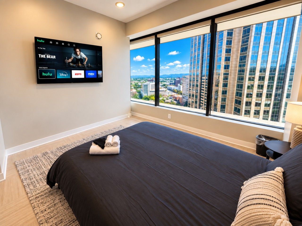 Une chambre d’hôtel avec un grand lit, un téléviseur fixé au mur et une vue sur la ville grâce à de grandes fenêtres.
