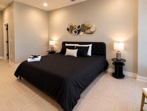 A bedroom with a large bed, two bedside tables with lamps, a wall art piece, and a door. - Skyline Escape | 3BR + King Bed (Birmingham)