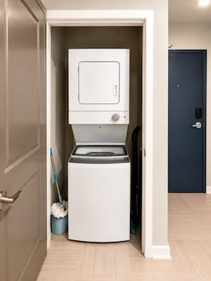 A compact laundry room with a washing machine and dryer, a mop, and a broom. - Skyline Escape | 3BR + King Bed (Birmingham)