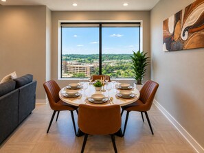 A dining area with a round table set for four, a sofa, and a large window with a city view. - Skyline Escape | 3BR + King Bed (Birmingham)