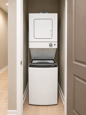 A compact, wall-mounted washer and dryer unit in a hallway with a wooden floor. - The Birmingham View | Spacious 2BR (Birmingham)