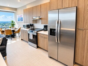 A modern kitchen with stainless steel appliances, wooden cabinets, and a dining area with a view. - The City Glow | Spacious 2BR | 2 Queens (Birmingham)