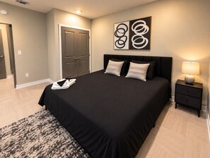 A bedroom with a large bed, a bedside table, a wall art piece, and a door. - Downtown View Retreat | 3BR | 2 Kings (Birmingham)