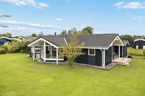 A single-story house with a covered porch and a small deck, surrounded by a well-maintained lawn. - Cosy, modern holiday home in a lovely area (Juelsminde)