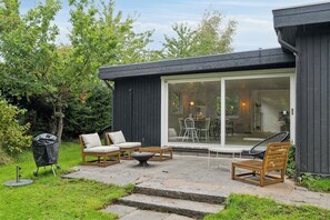 Eine Terrasse mit Gartenmöbeln, einem Grill und einer Glasschiebetür zu einem Innenbereich.