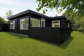 Ein modernes, schwarzes Haus mit großen Fenstern und einem umzäunten Garten.