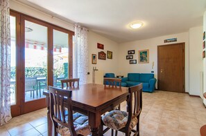 A dining area with a wooden table and chairs, a blue sofa, and a sliding glass door leading to an outdoor patio. - Kedimore - GoldenHouse Lazise (Lazise)