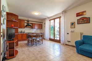 A kitchen with wooden cabinets, a dining table with chairs, a television, and a blue sofa. - Kedimore - GoldenHouse Lazise (Lazise)