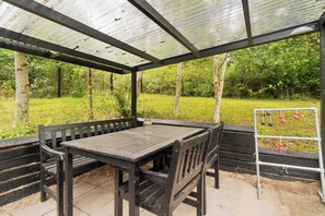 A covered outdoor seating area with a table and benches, surrounded by greenery. - Lovely house on Helgenæs (Knebel)