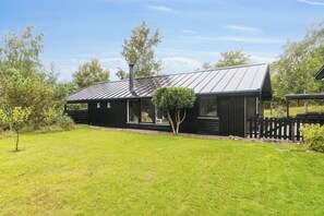 Une maison moderne avec un toit en métal, de grandes fenêtres et une cour clôturée.