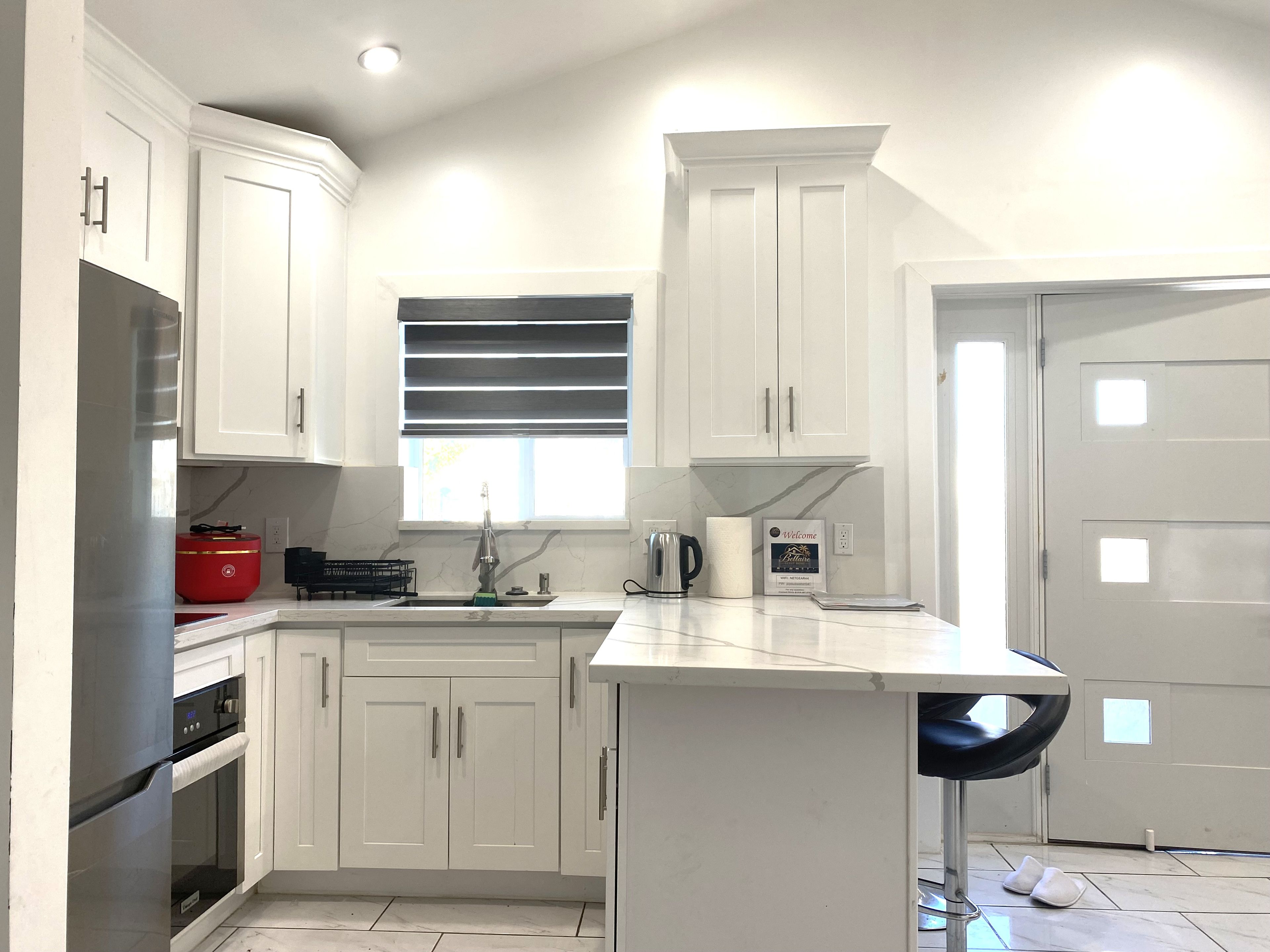 A modern kitchen with white cabinetry, a built-in oven, a red appliance, and a window with blinds.