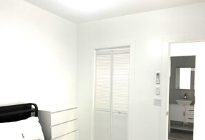 A room with a bed, a white wardrobe, a door with a window, and a bathroom visible through an open door. - Modern Comfort Meets Luxury — Your Stylish North Hollywood Getaway (NORTH HOLLYWOOD)