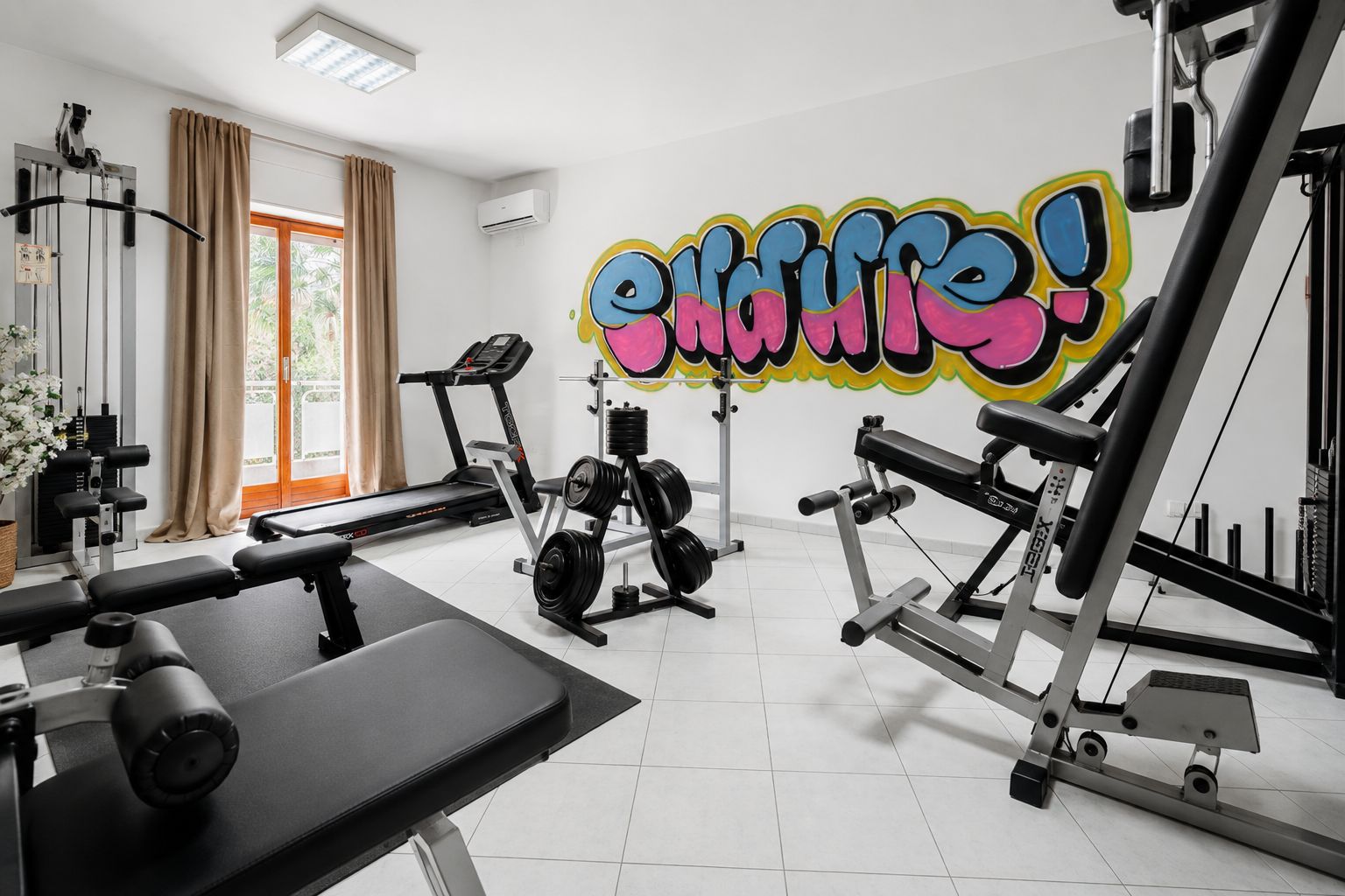 Un gimnasio con equipo de ejercicio, una cinta de correr y una pared con un diseño de grafiti colorido.