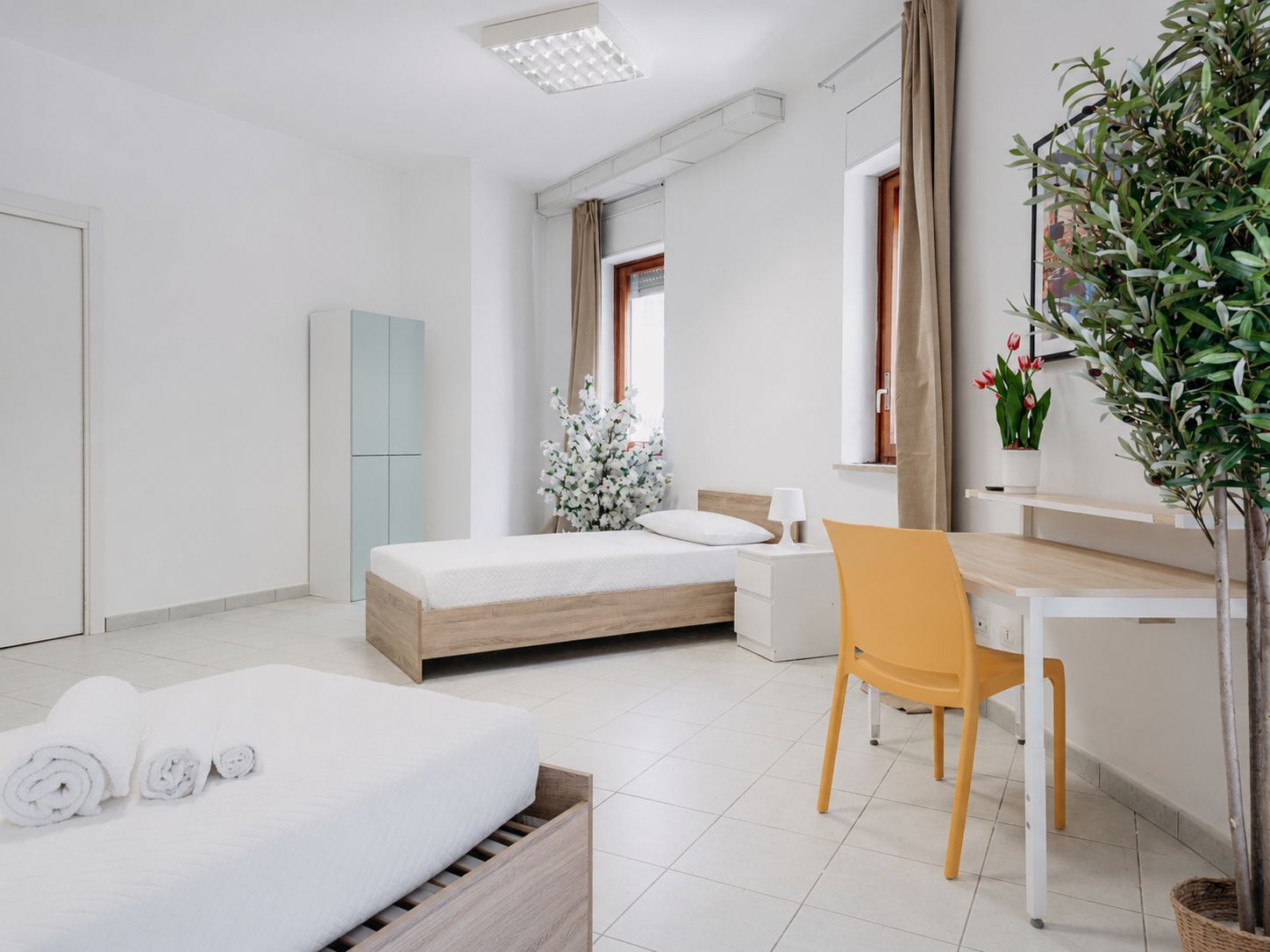 Una habitación de hotel moderna con cama, escritorio, silla, armario y una planta en maceta.