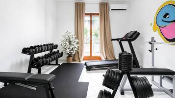 Ett gym med träningsutrustning, ett löpband och ett stort fönster med gardiner.
