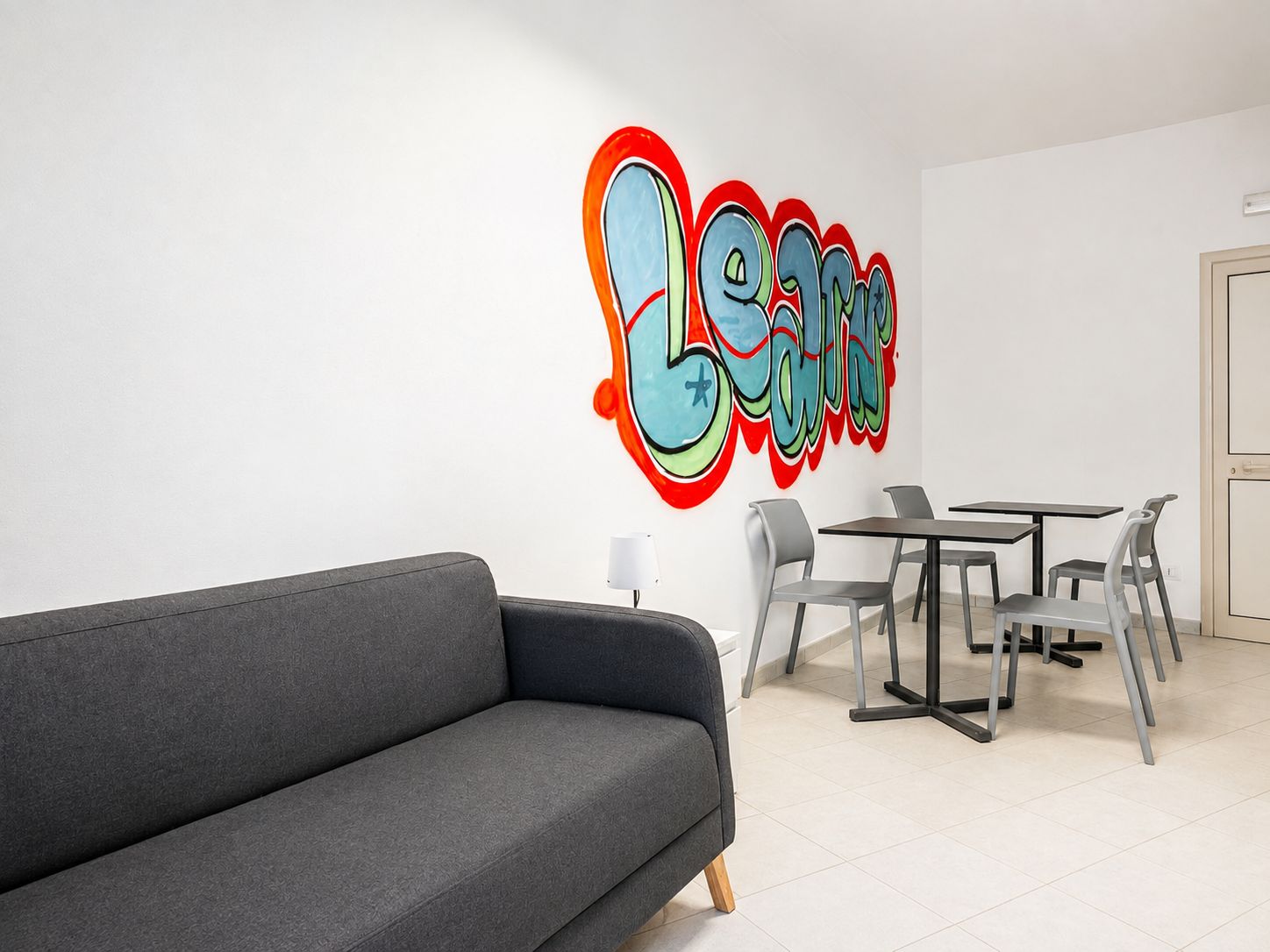 Un interior moderno con un sofá gris, una mesa de comedor con sillas y una pared con grafitis de colores.
