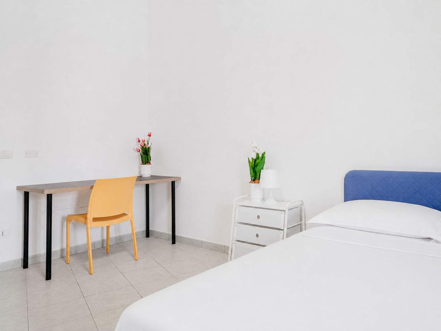 Ein Hotelzimmer mit einem Bett, einem Schreibtisch mit Stuhl, einem Nachttisch mit Lampe und einer Zimmerpflanze.
