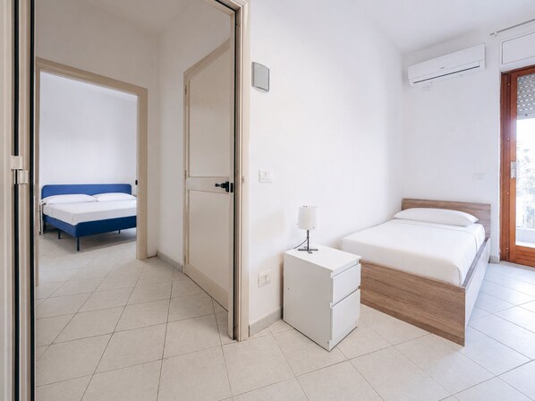 A hotel room with a bed, bedside table, and an air conditioning unit.