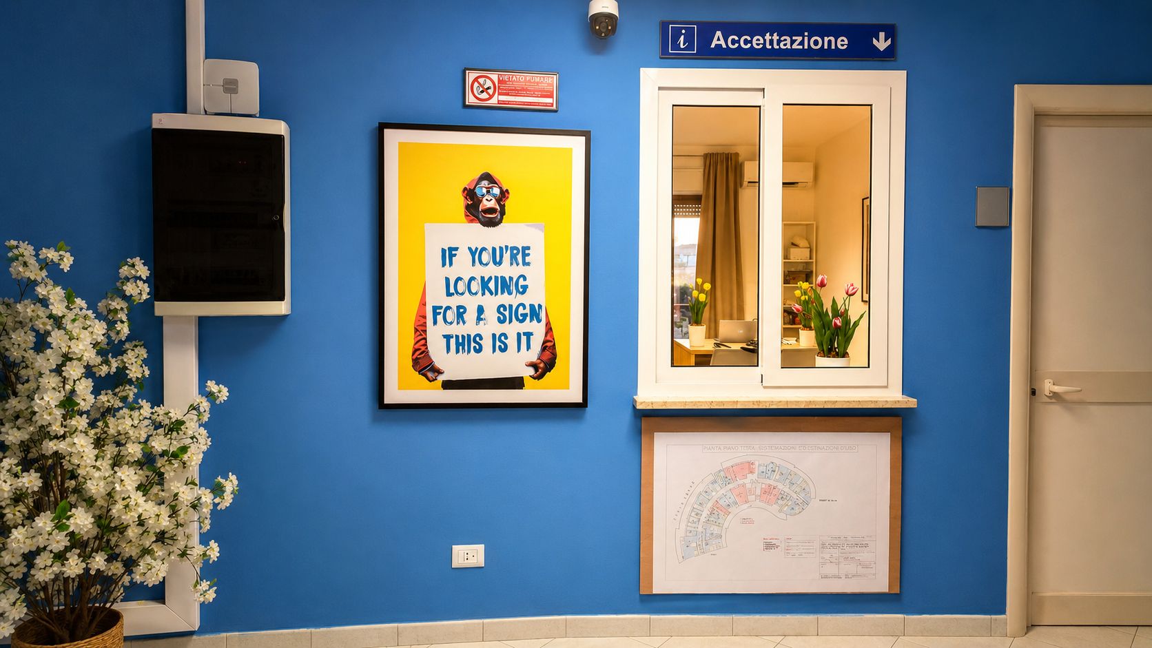 Un espace d’accueil avec un panneau indiquant le comptoir de réception, un cadre représentant un singe tenant un panneau, et un plan des lieux affiché au mur.