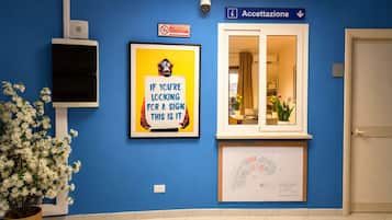 Un espace d’accueil avec un panneau indiquant le comptoir de réception, un cadre représentant un singe tenant un panneau, et un plan des lieux affiché au mur.