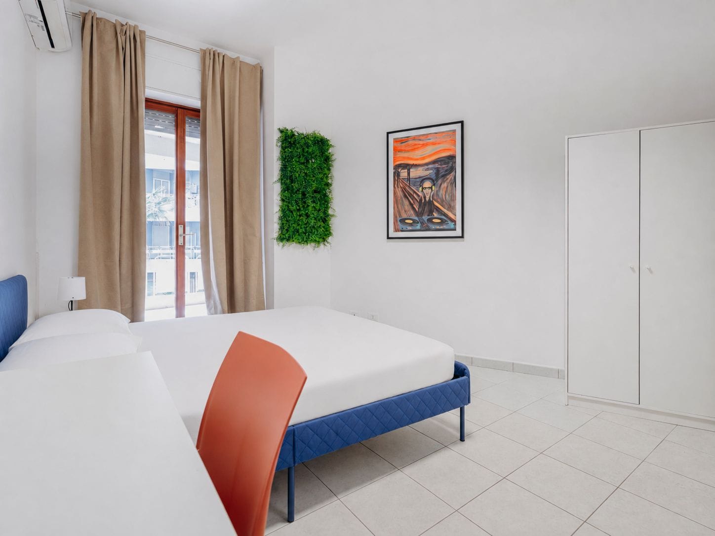 A hotel room with a bed, a wardrobe, a wall-mounted plant, and a framed picture.