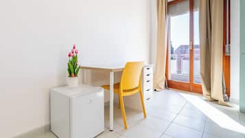 Une petite pièce propre, avec un mini-réfrigérateur blanc, une chaise jaune, un bureau blanc et une plante en pot.