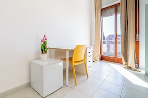 A small, clean room with a white mini-fridge, a yellow chair, a white desk, and a potted plant.