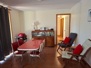 A dining area with a red table and chairs, a wooden cabinet with glassware, and a red grill.