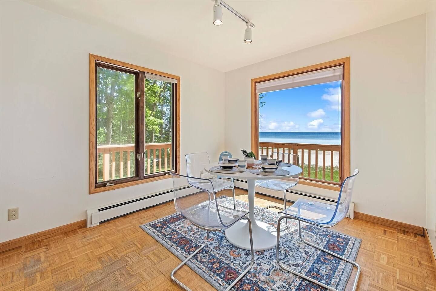 Un área de comedor con una mesa y sillas, ventanas amplias con vista a la playa y suelo de madera.