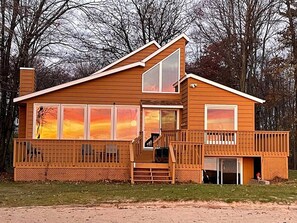 A two-story wooden cabin with a balcony, large windows, and a front porch.