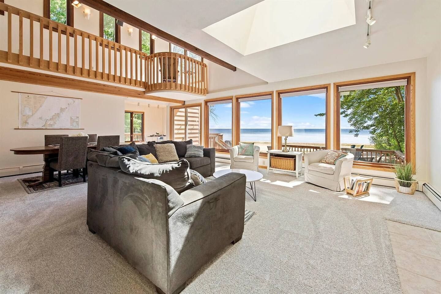 A spacious living area with a high ceiling, large windows offering a view of the sea, and a balcony overlooking the ocean.