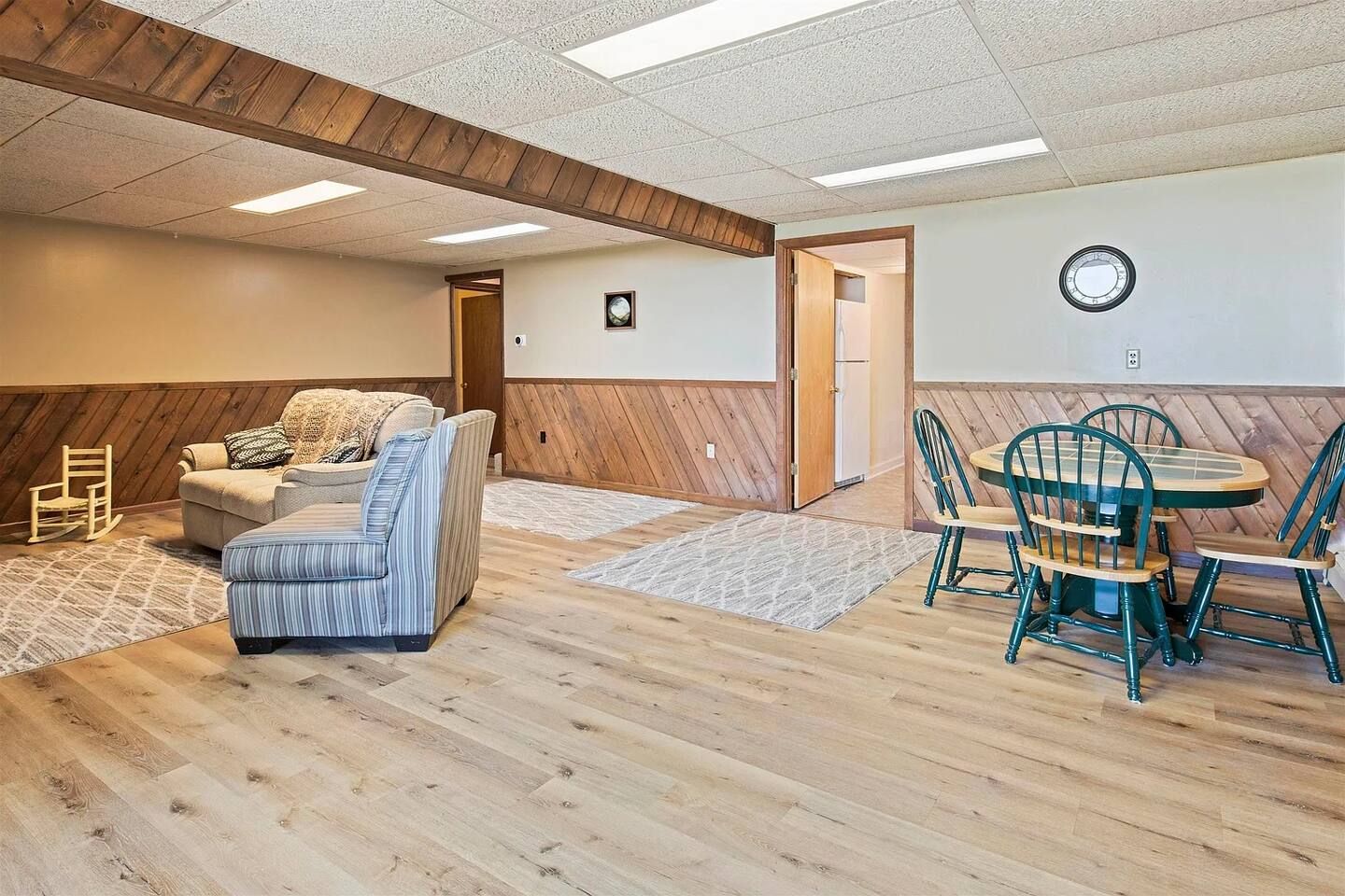 A room with a wooden floor, a striped sofa, a dining table with chairs, and a clock on the wall.